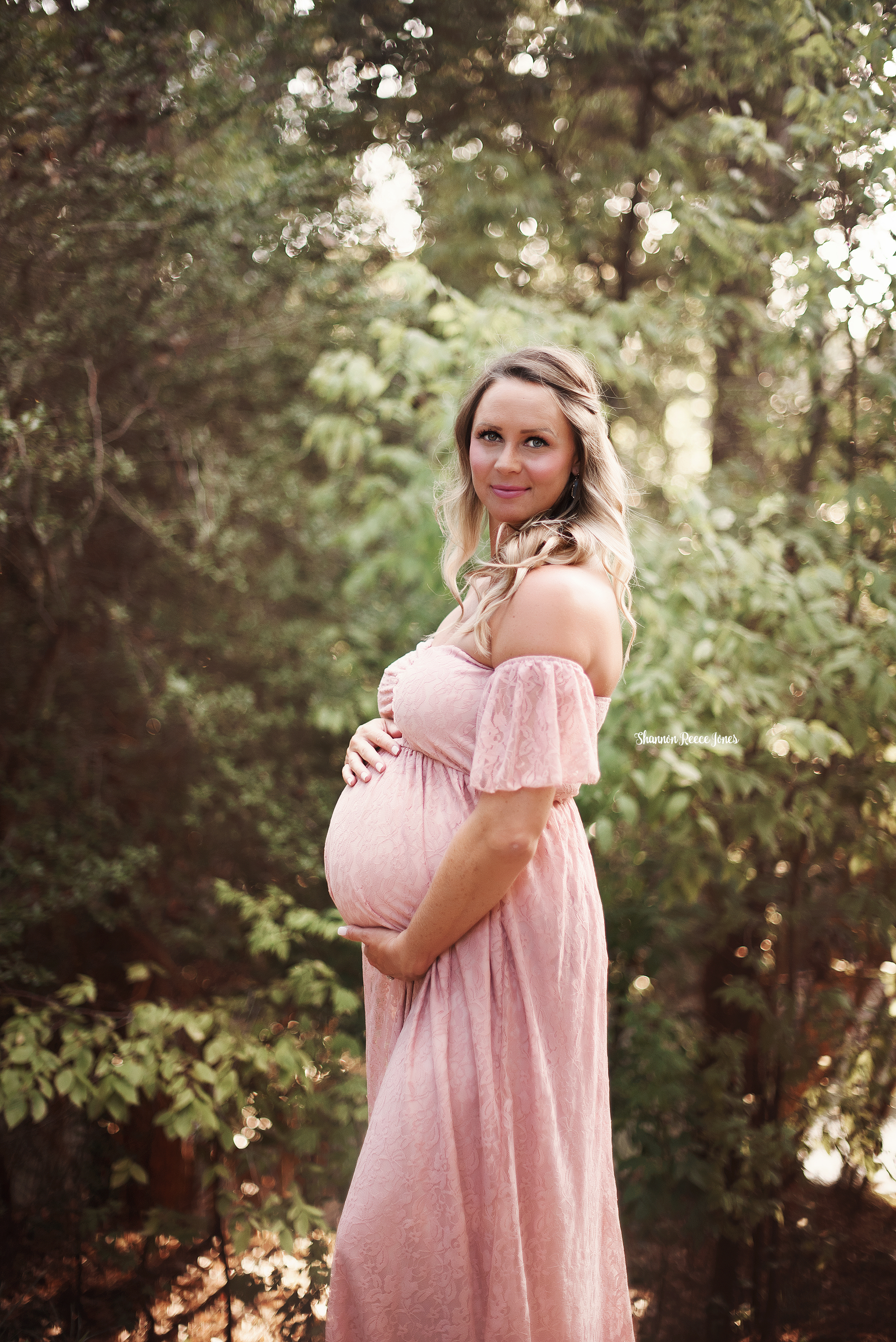 woman in pink maternity dress posing in front of trees