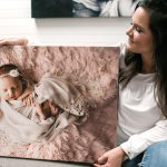 Newborn photographer holding canvas of baby girl asleep in swaddle