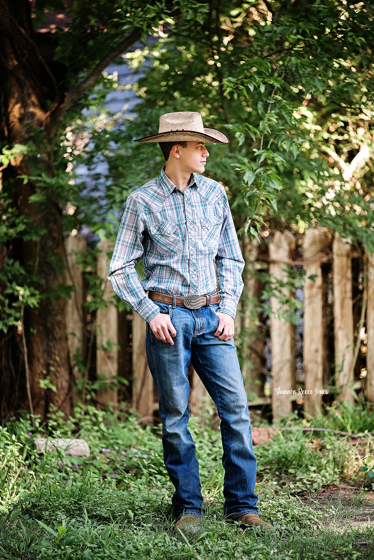 high school senior boy in cowboy hat standing against fence