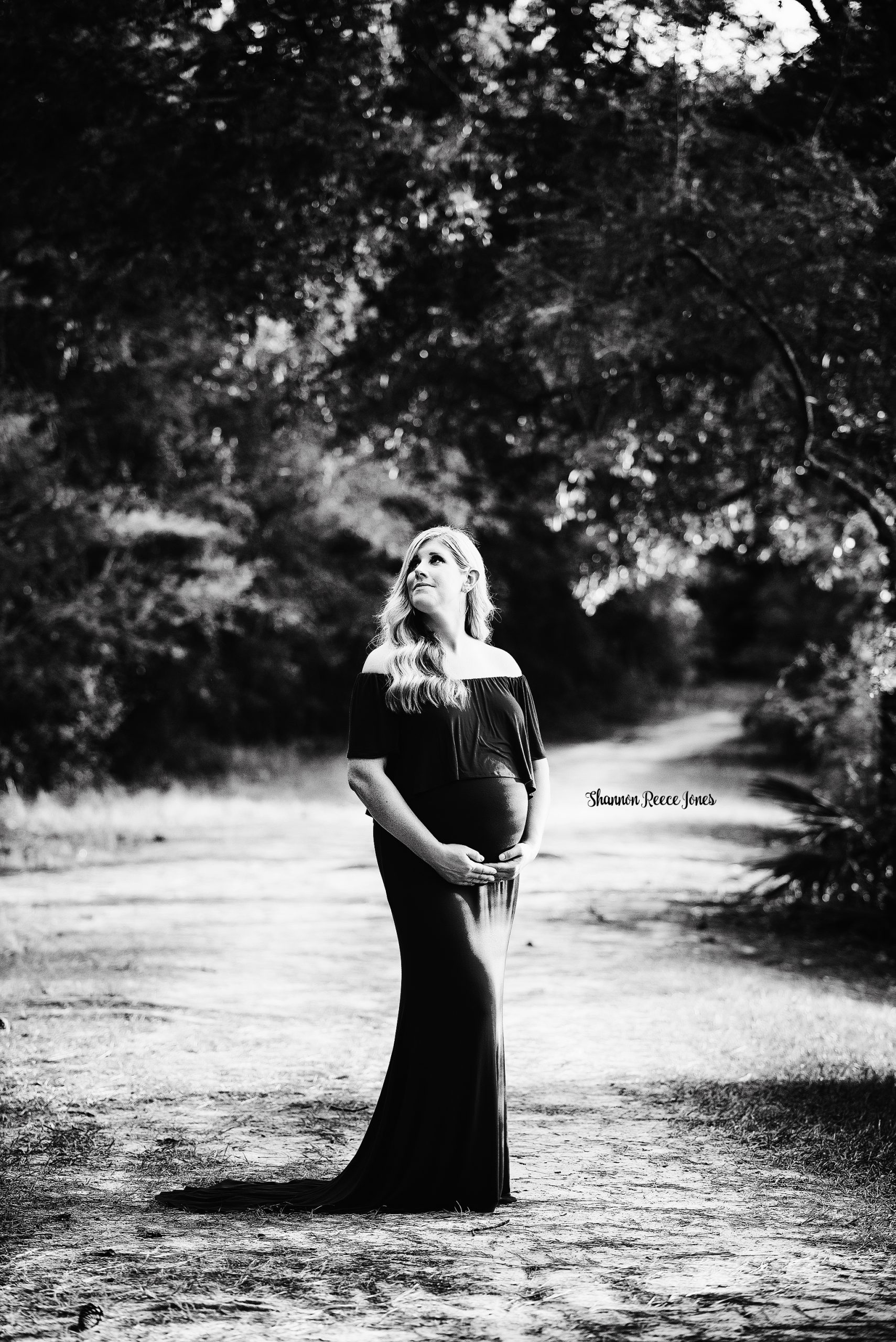 black and white image of woman in maternity dress looking up at trees
