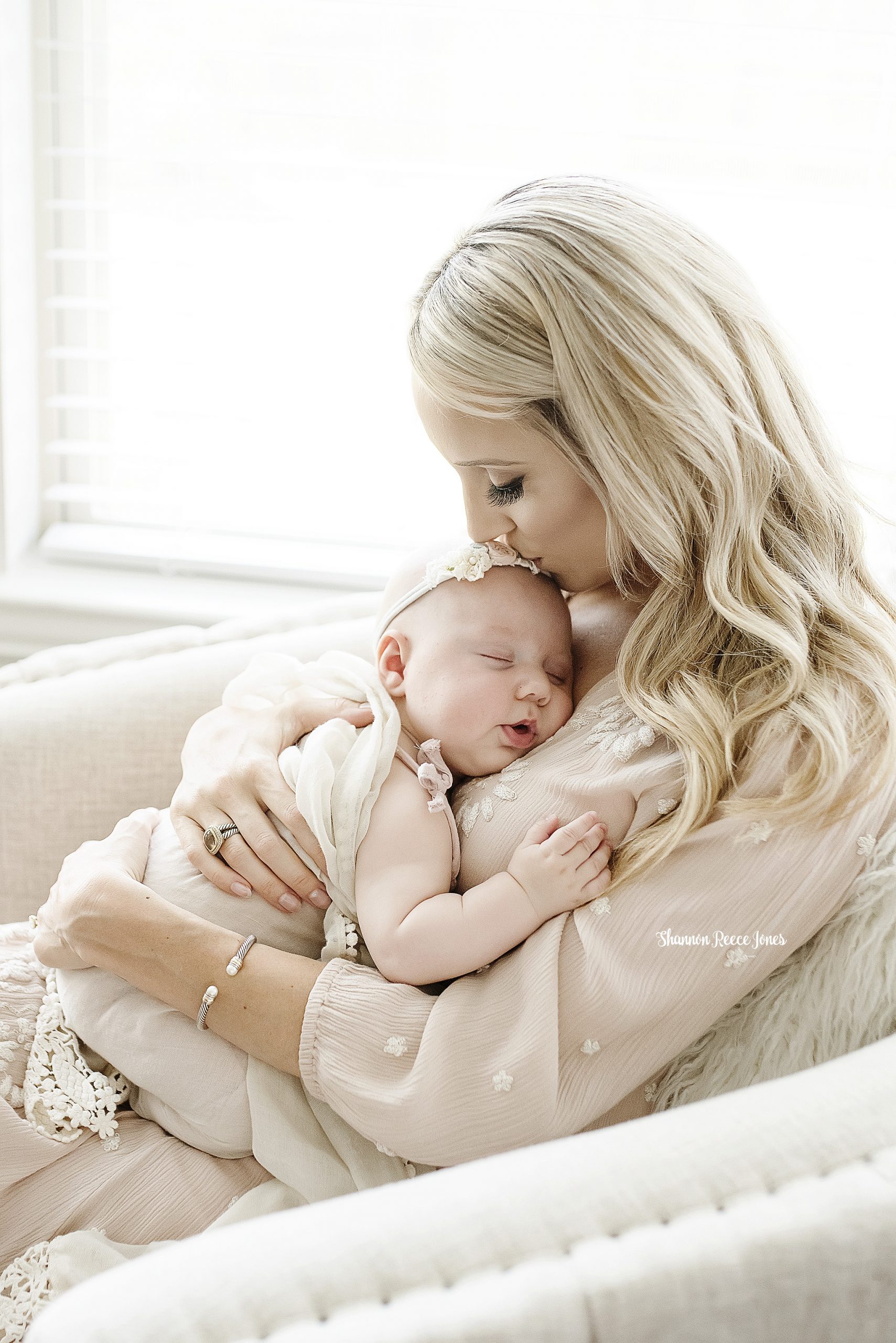 houston baby and family photographer, mom seated by window kissing sleeping baby 