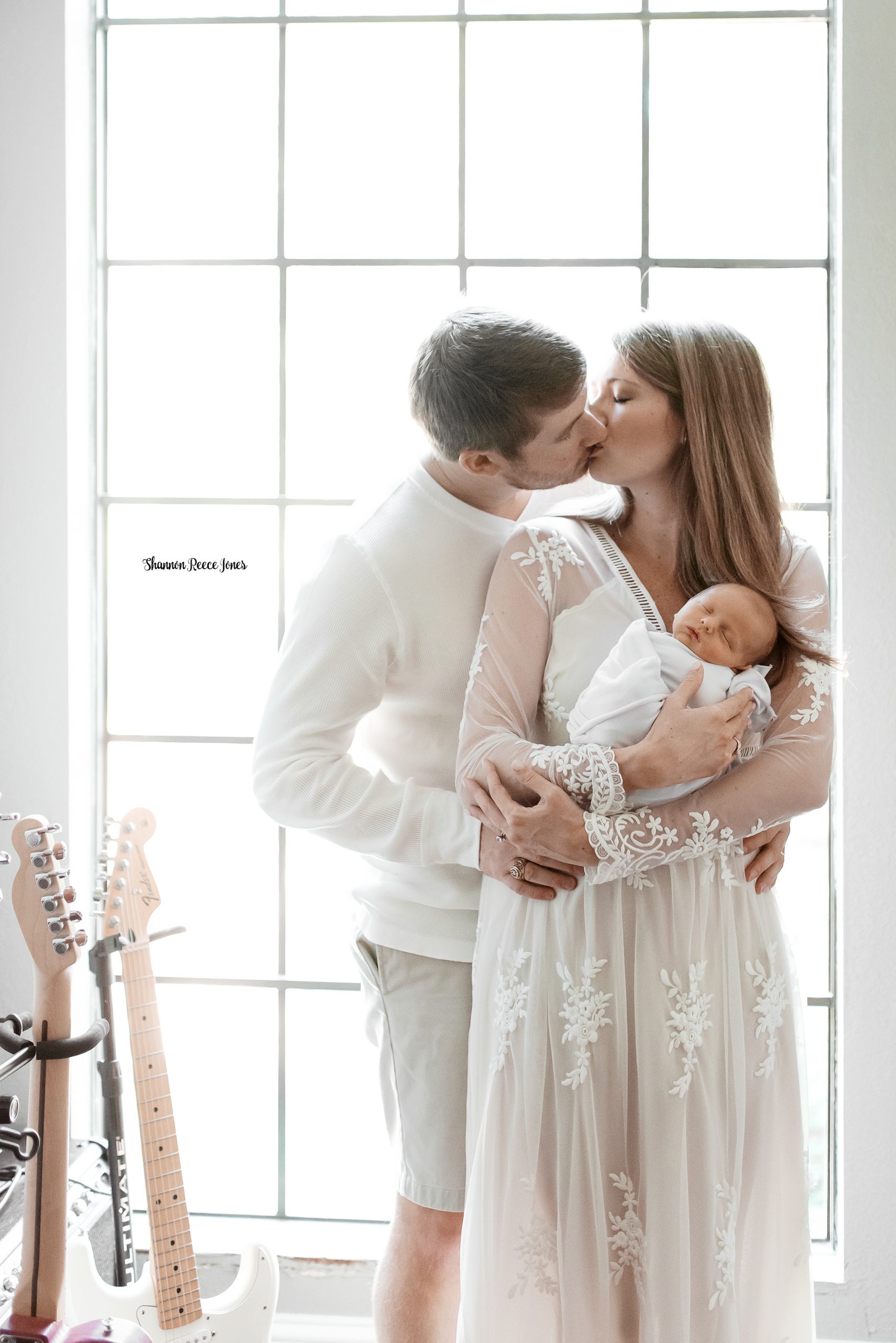 at-home baby pictures, parents standing by window kissing with baby in arms