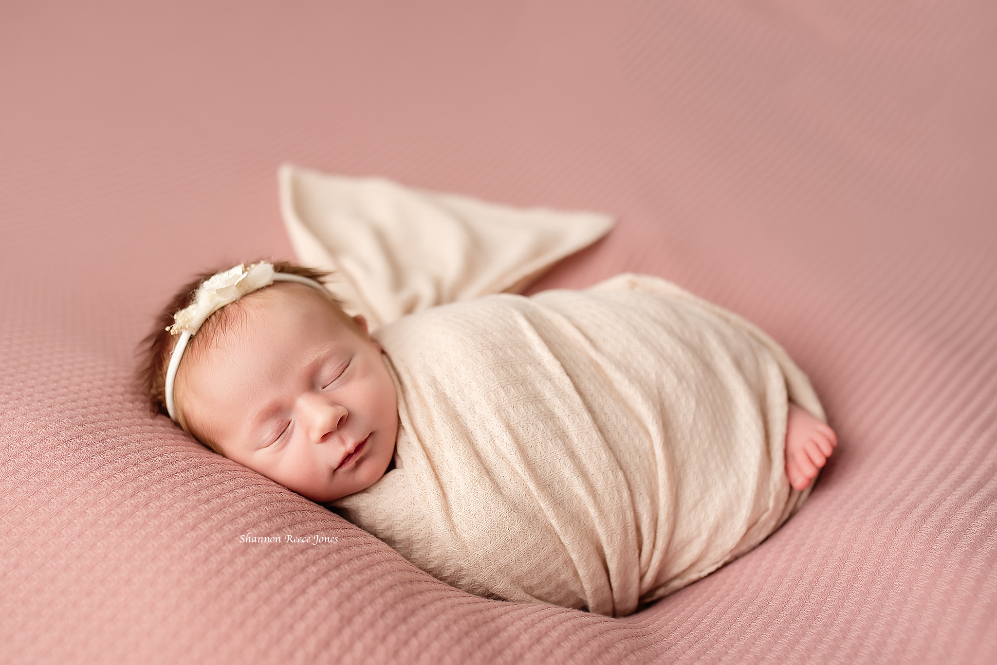 infant in headband and pink swaddle