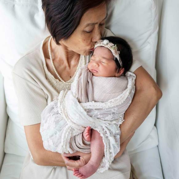 Grandma holds newborn close as she kisses the top of baby's head