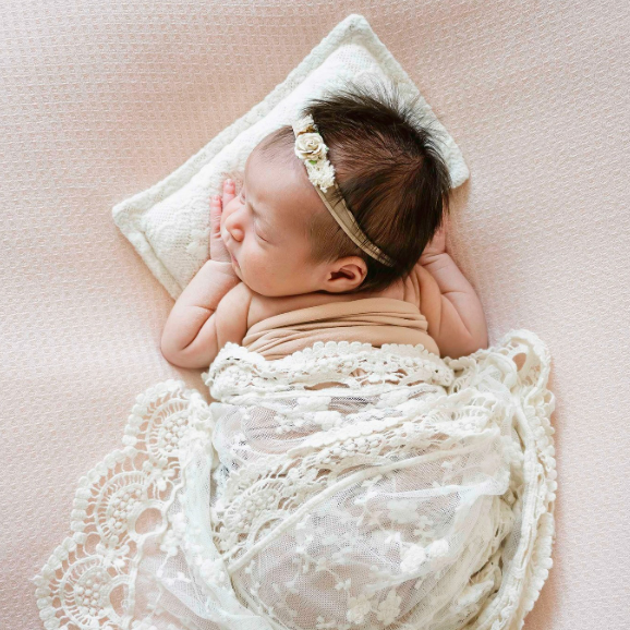 Newborn baby asleep on pillow with lacy blanket in Houston photo studio