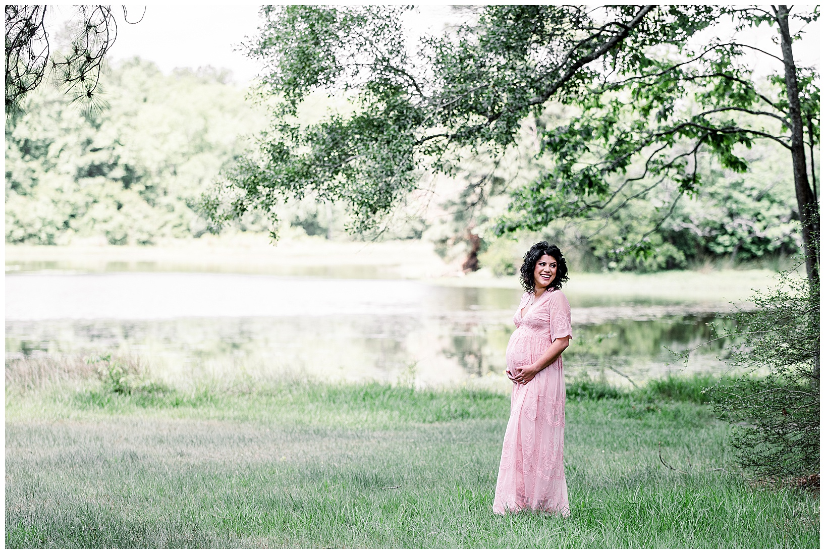 Woman in pink maternity gown standing by lake in Conroe