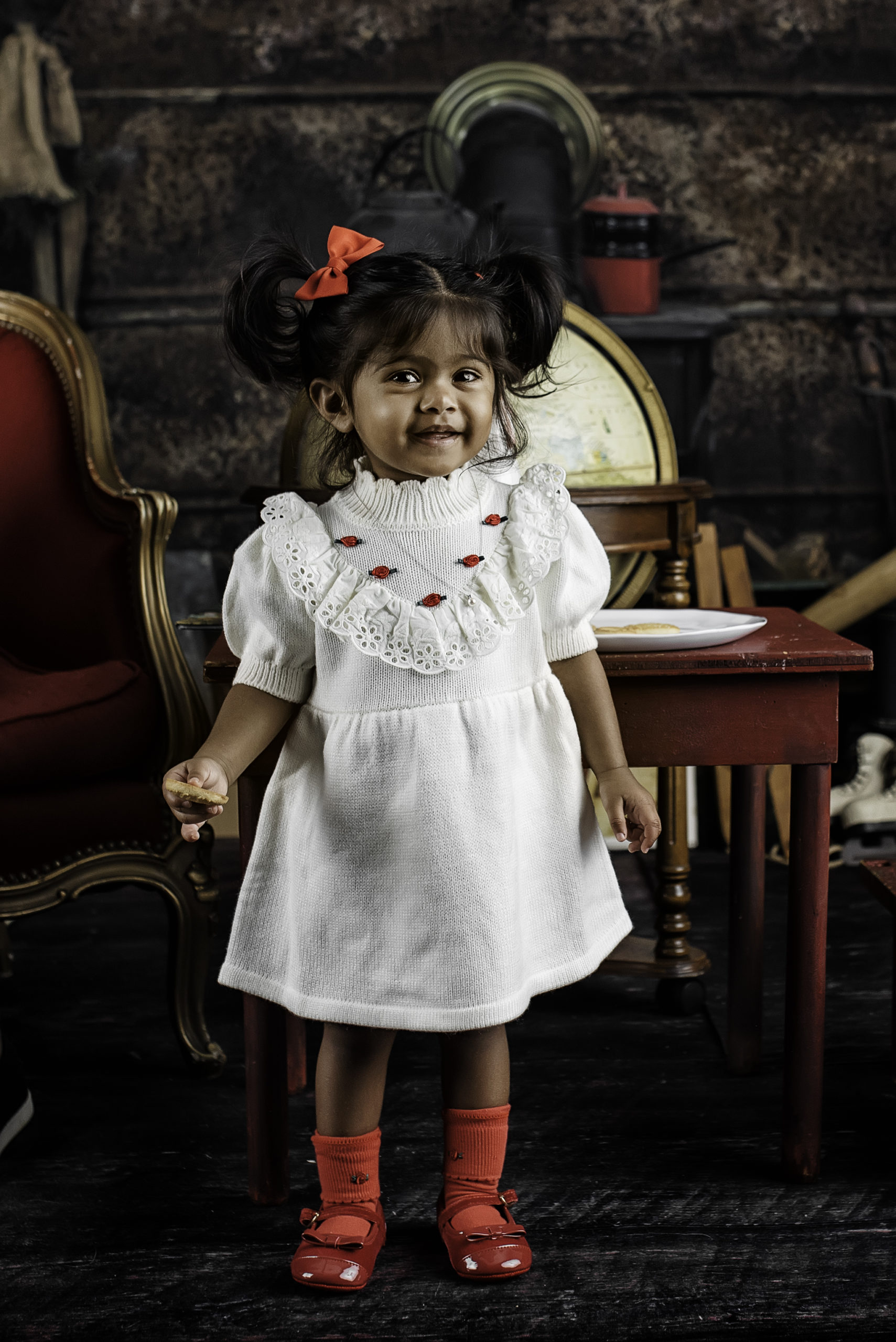 little girl in white dress and red shoes against Christmas backdrop