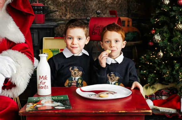 Two little boys eating milk and cookies with Santa beside them