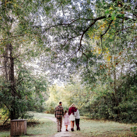 Family in festive sweaters walking together under the trees in a Houston Texas park