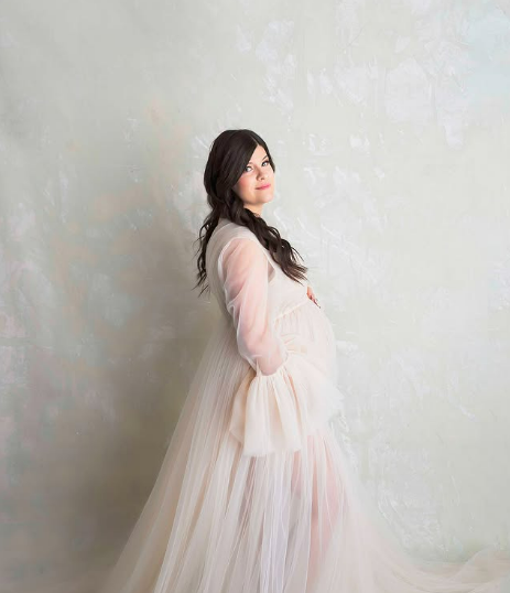 Maternity studio portrait of woman in flowing white dress against a pretty canvas backdrop