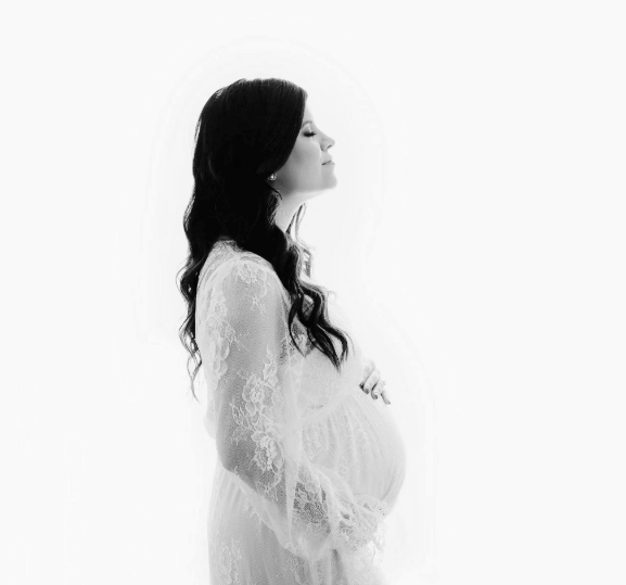 Natural light black and white silhouette of dark-haired woman in white lace maternity gown