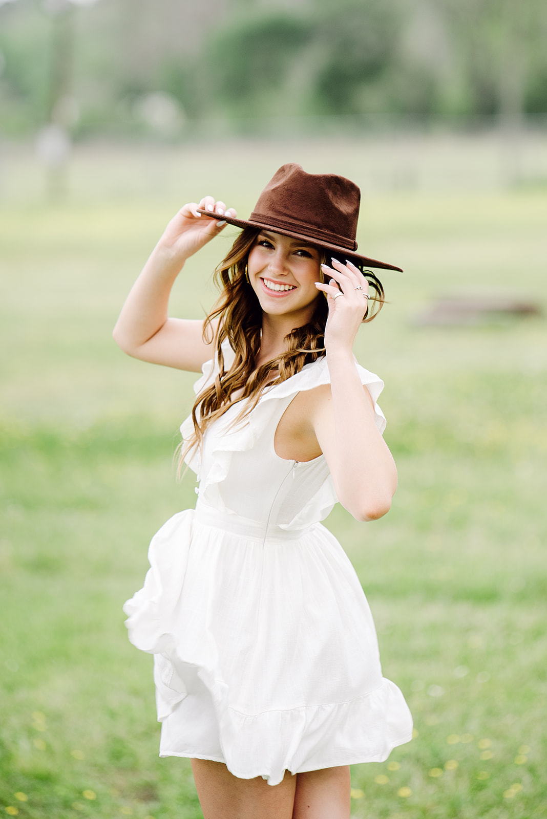 what to wear for your senior photography session, high school girl in white dress, brown boots, and cowboy hat standing in field