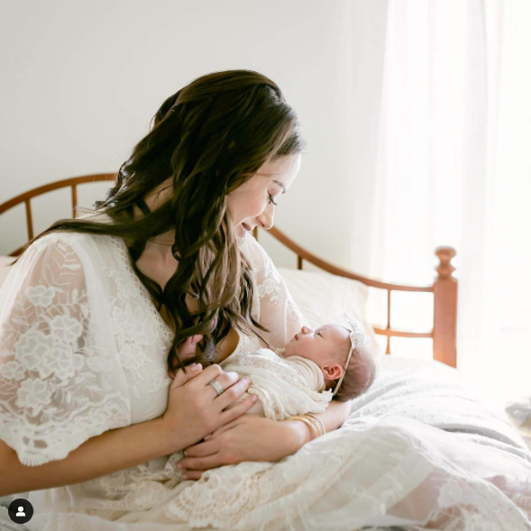 Mother cradling baby on bed during at home newborn photography session in Texas - Houston Newborn Photographers