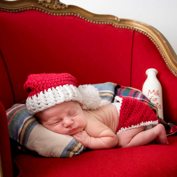 Newborn baby asleep in Santa's chair with bottle of milk