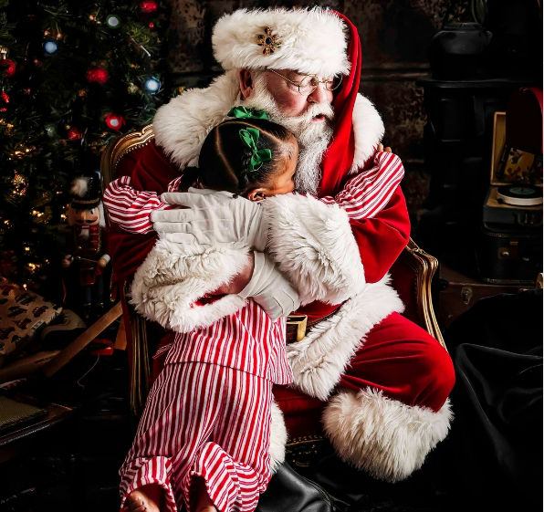 Girl in red and white striped pajamas hugging Santa Claus