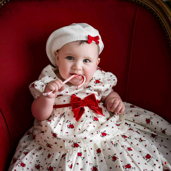 Baby girl in red and white dress sucking on candy cane