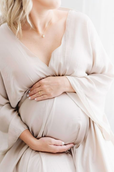 Woman in flowing maternity gown with hands cradling her belly