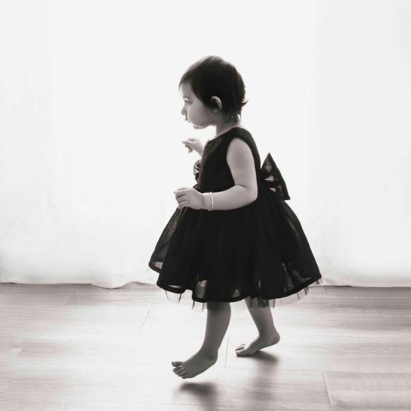 Toddler girl in tulle black dress and bracelet tiptoes across the floor