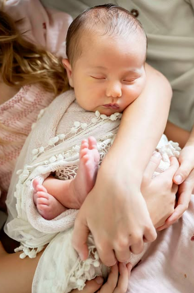 Baby in pretty cream swaddle nestles peacefully in her big sister's arms