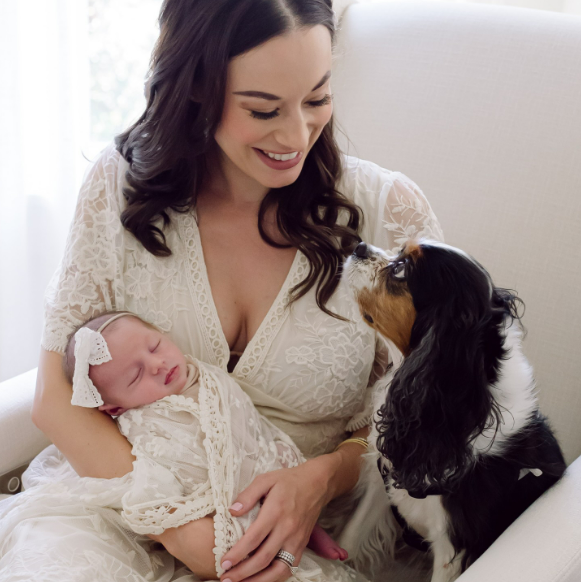 Mother holding newborn with dog seated next to her, by Houston's best in-home newborn photographer