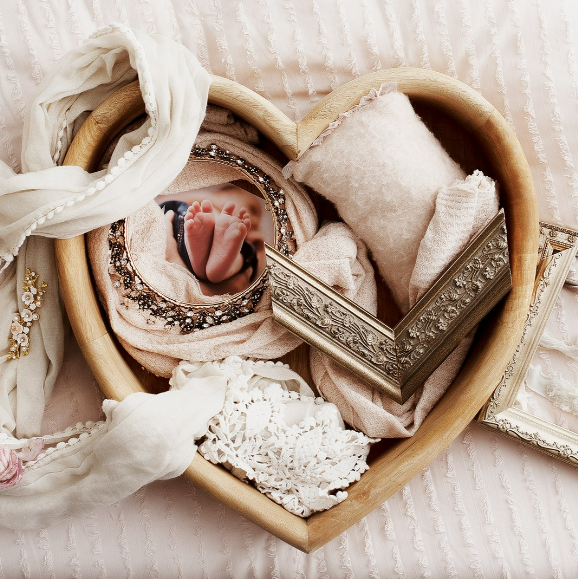 Printed newborn photo and frame sample artfully arranged with wooden heart prop and elegantly draped cloth