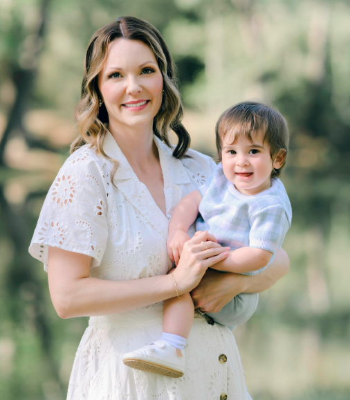 Mom holding her toddler son on her hip as they stand together in a sunny park in Houston Texas