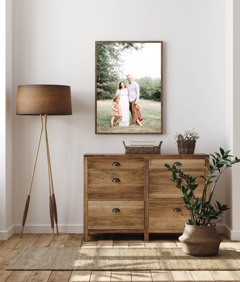 Framed canvas print of Houston family, hung over a chest of drawers with a lamp and potted plant