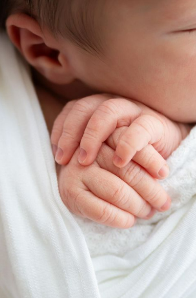 Detail of baby's hands tucked under their chin