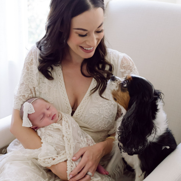 Spaniel dog looks up at woman as she sits holding newborn baby during an at home session in Houston Texas