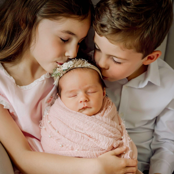 Little boy and girl kissing the top of their new baby sister's head