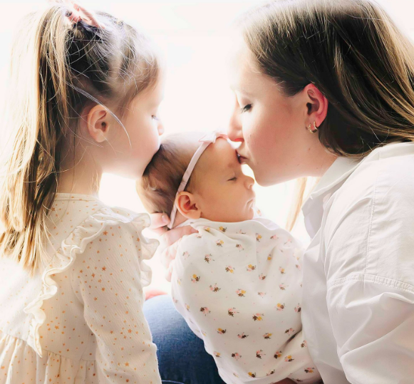 Happy new year photo of mom and big sister kissing swaddled newborn