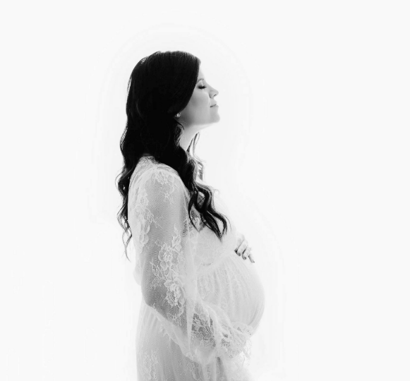 Black and white image of dark-haired woman in white maternity gown in Houston studio