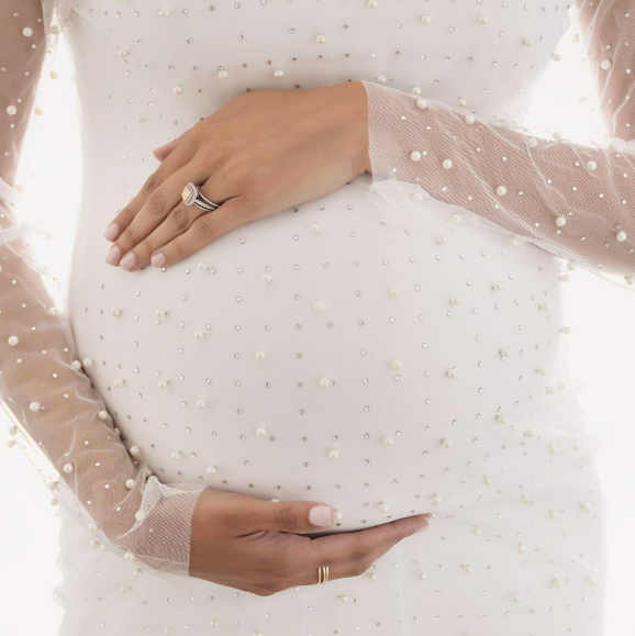 Woman in pearl-studded maternity gown with hands cradling her baby bump