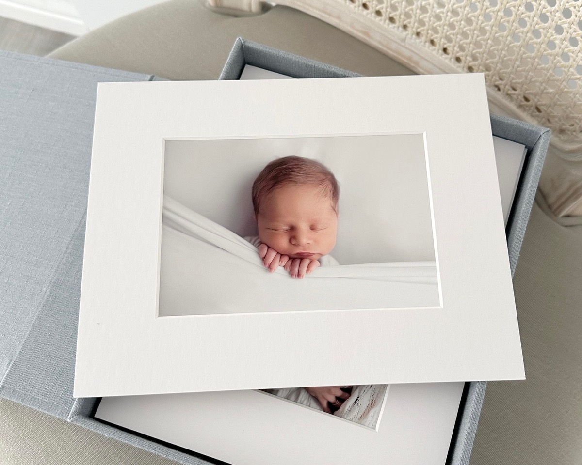 Matted print of sleeping newborn in a blue linen keepsake box in boutique studio near Houston Texas