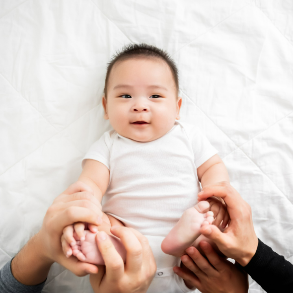 Baby boy in white onesie lying on his back while mom and dad play with him, illustrating a post about music classes for Houston babies and families