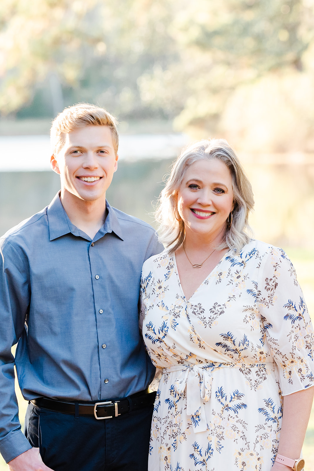 Young man in a blue-button up shirt stands with his arm around his mom during a high school senior photoshoot near Houston Texas