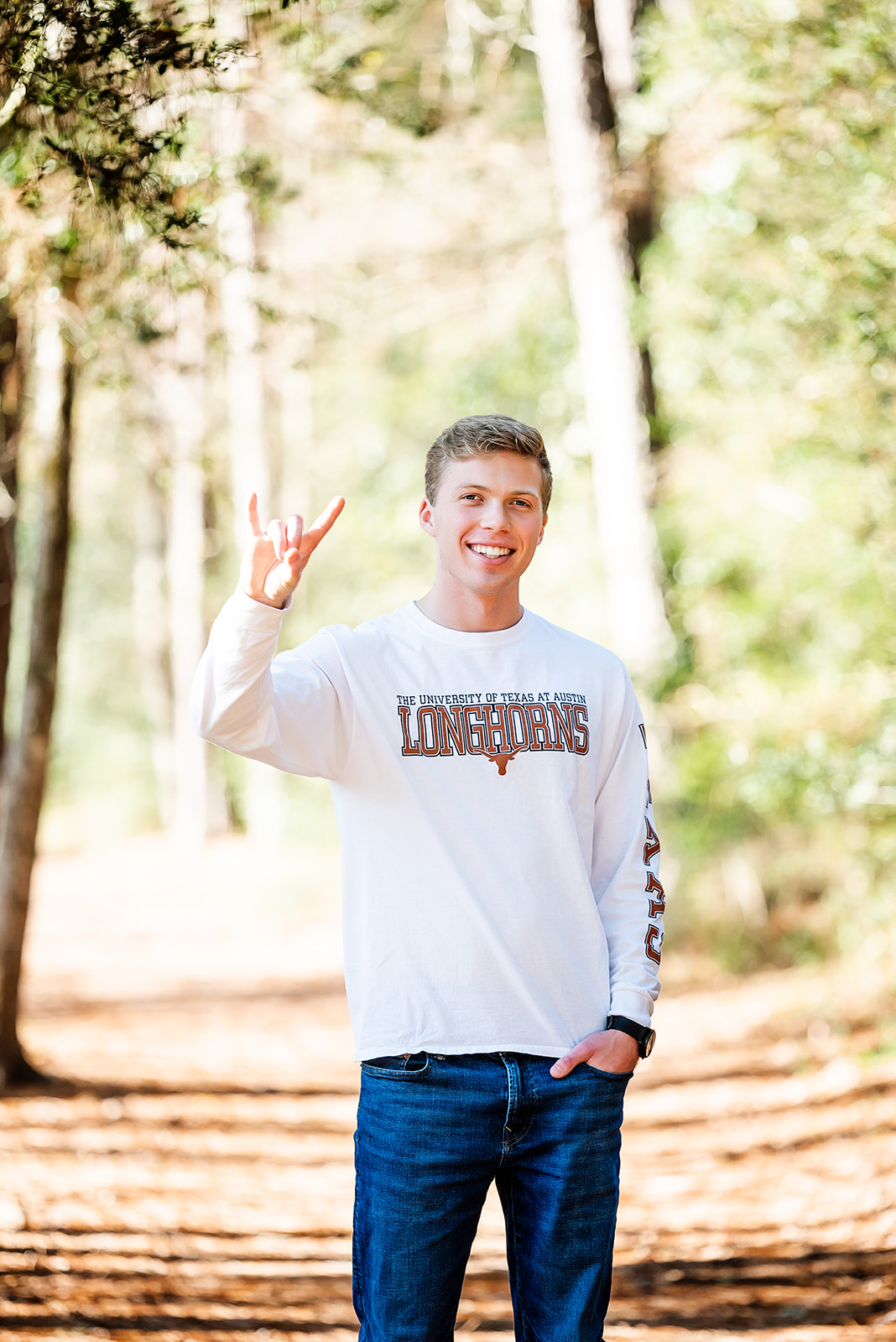 Smiling high school senior wearing a shirt with the University of Texas logo makes the Longhorns sign as he poses for his senior portraits