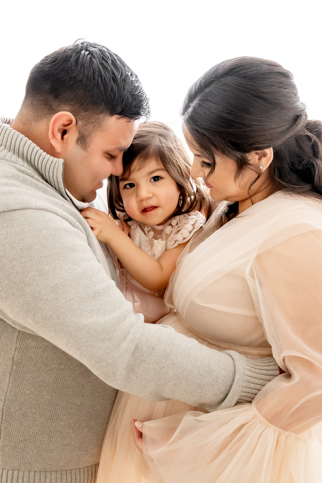 Mom and Dad hold their toddler daughter between them during a family maternity portrait