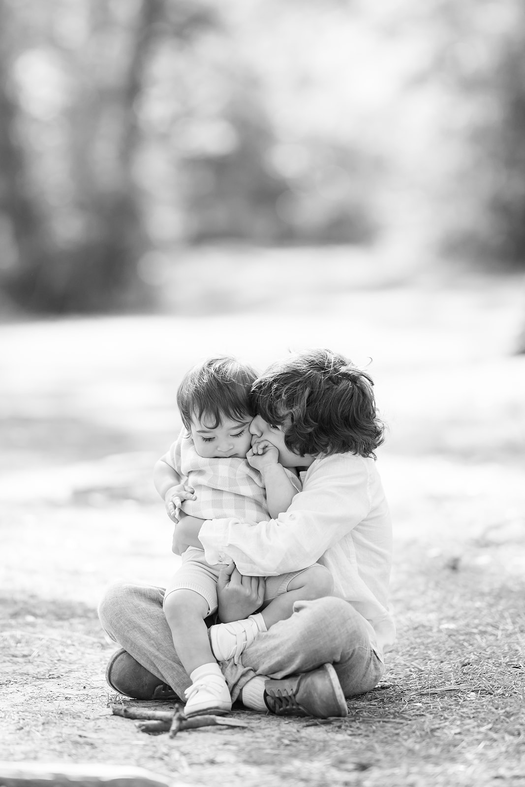 Little boy seated on the ground and pulling his toddler brother in for a tight hug and a kiss