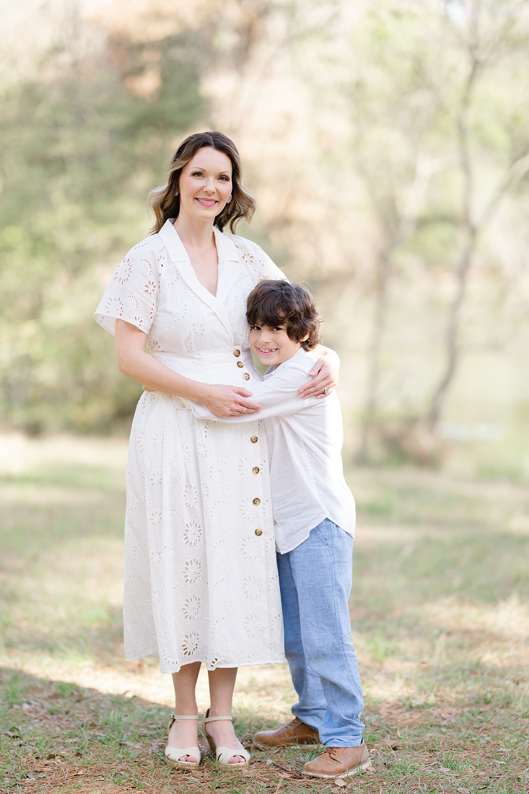 Mother and young son stand together with their arms wrapped around each other as they pose for a portrait