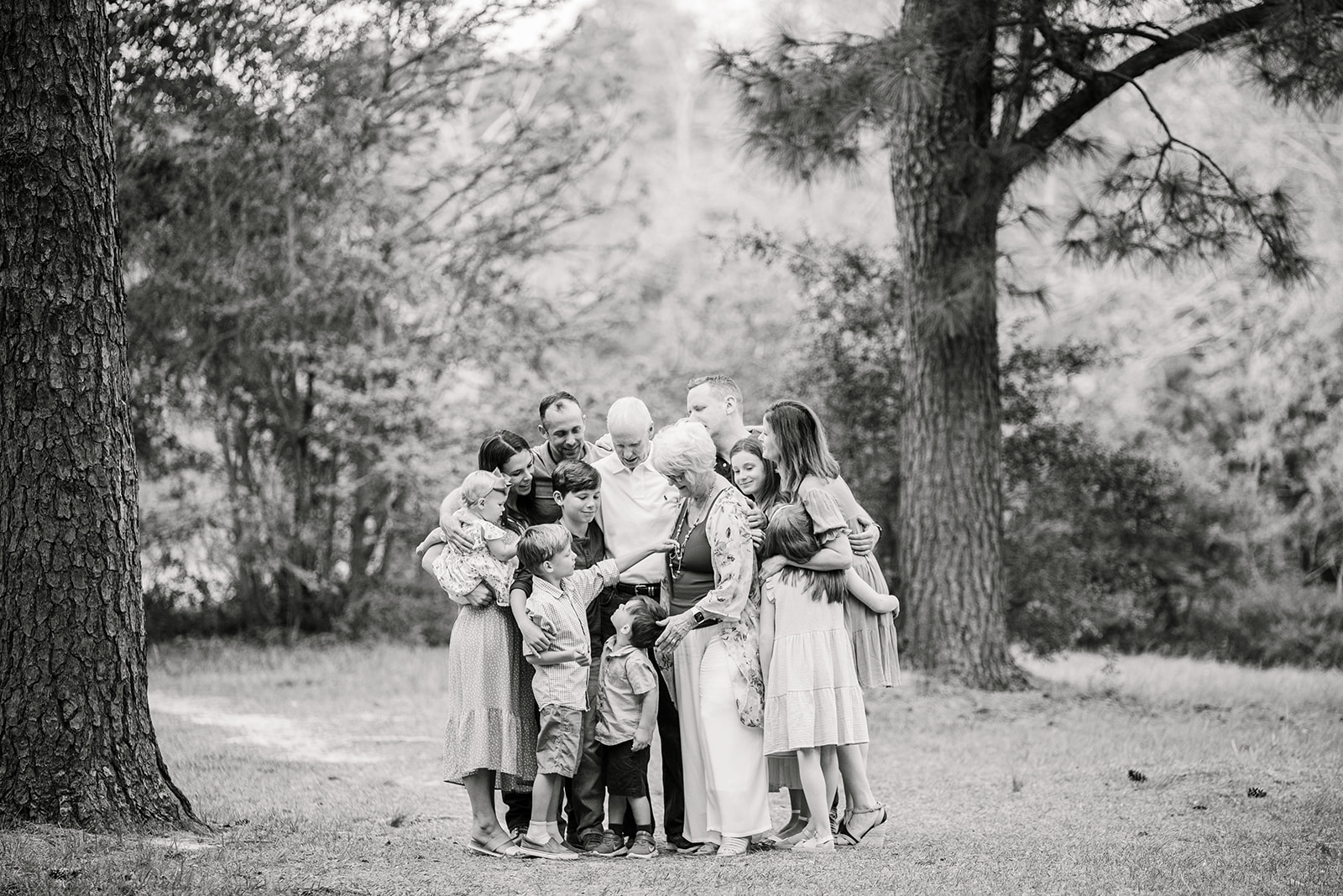 Black and white image of extended family gathered close to look over each other's shoulders as one of the little boys admires Grandma's necklace