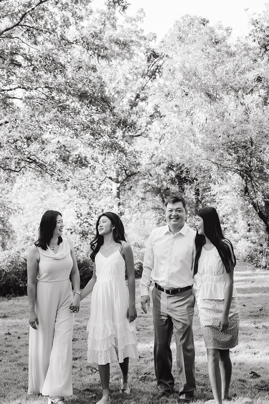 Black and white image of parents and teenage daughters talking and laughing together under the trees in a park in Houston Texas