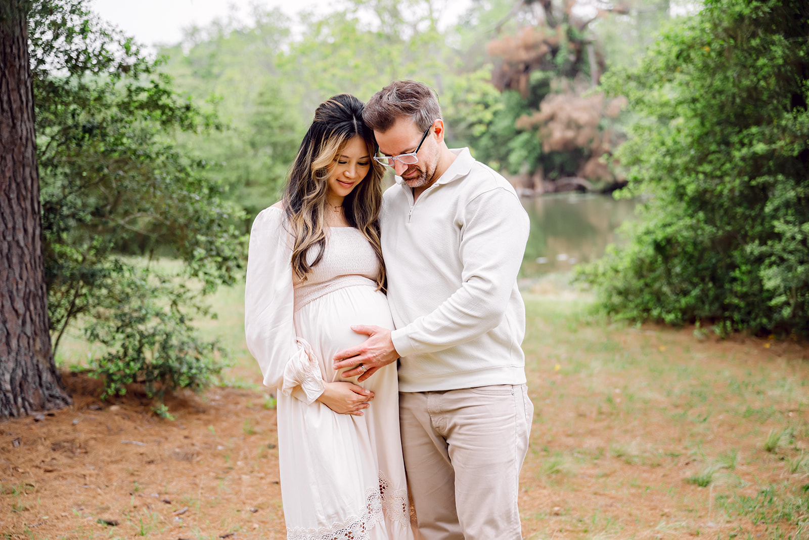 Couple standing together in a forest clearing, husband with his hand on his wife's baby bump, during a maternity photoshoot