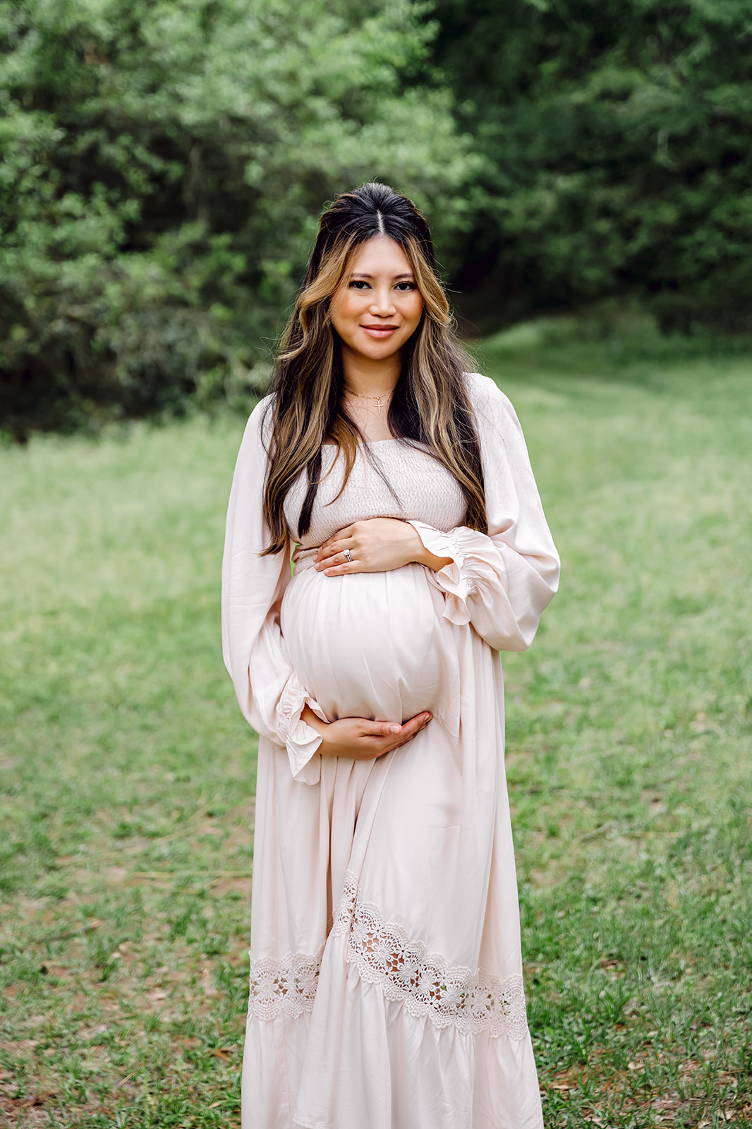 Mother in pale pink dress with her hands cradling her baby bump