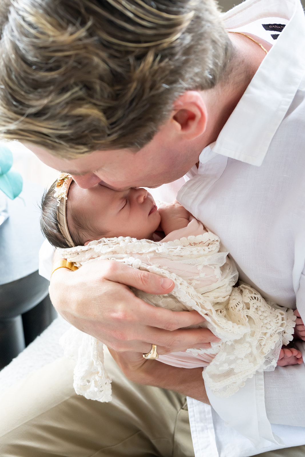 Dad bending down to kiss his sleeping newborn on the top of her head as she sleeps peacefully in his arms