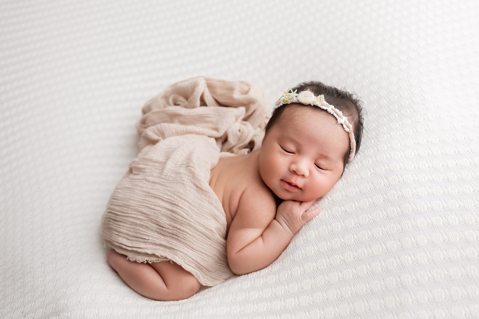 Newborn baby in soft wrap and headband sleeping peacefully during her newborn studio session