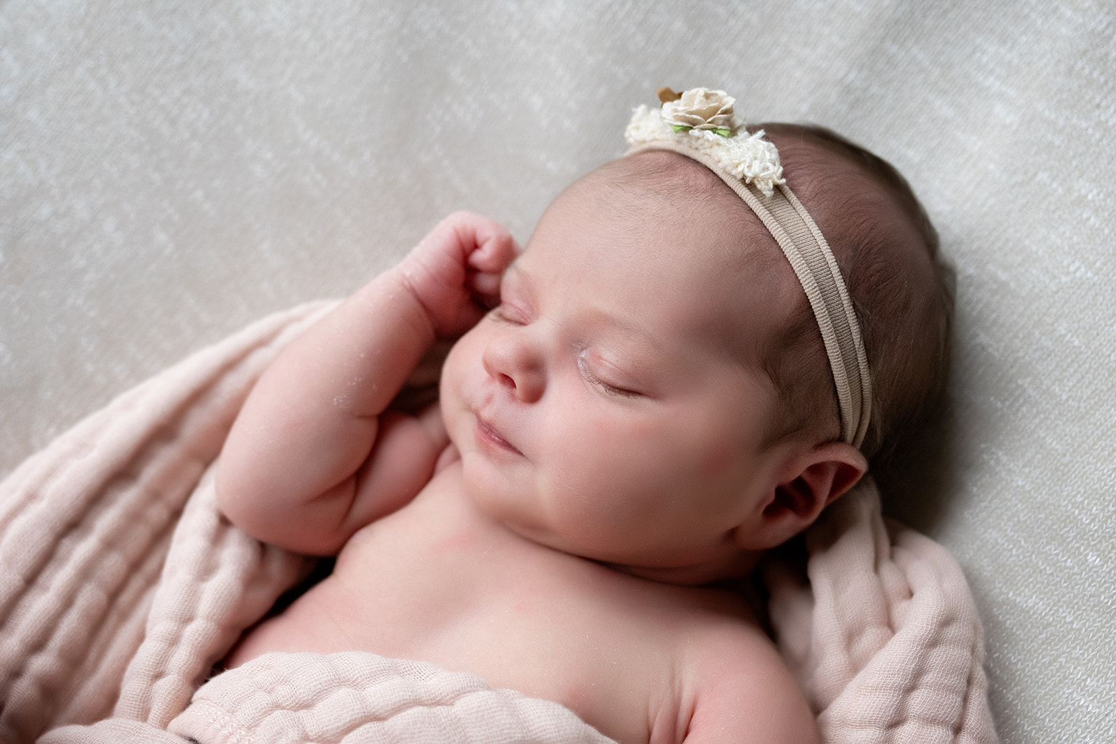 Newborn girl with floral headband asleep with her fist tucked against her cheek