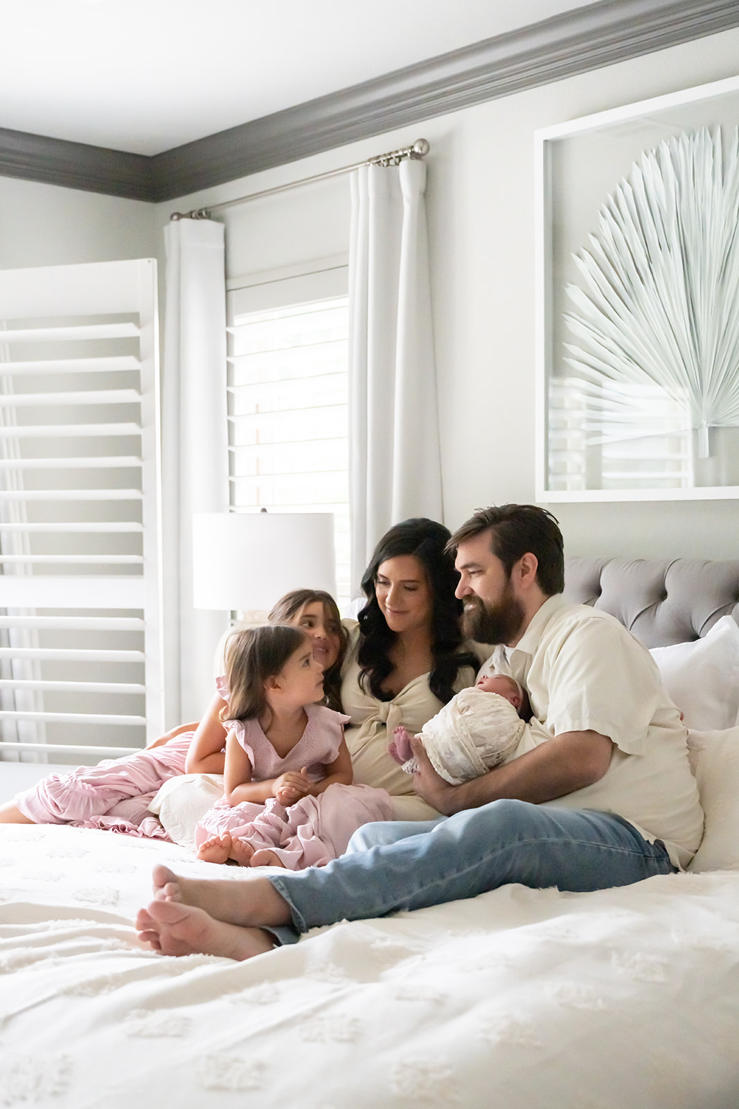 Family sitting on bed in a room glowing with natural light, looking down at newborn