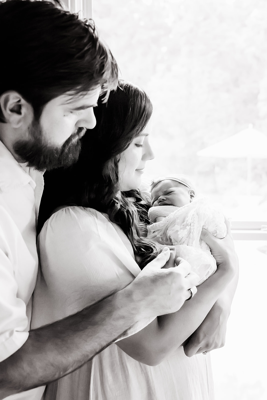 Mother holding newborn in her arms while Dad stands behind her with his arms around them both