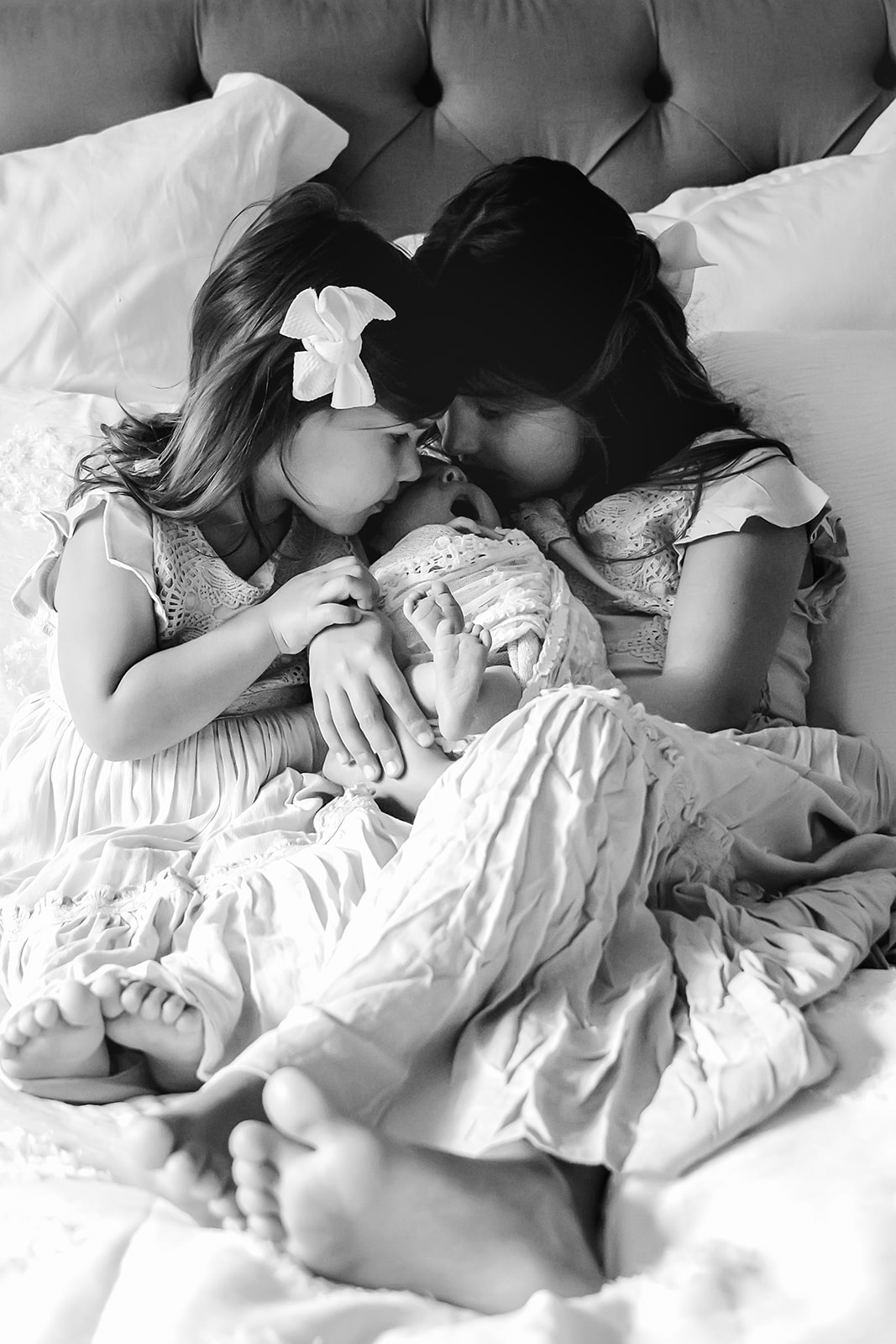 Black and white image of two little girls snuggling on the bed with their new baby sister